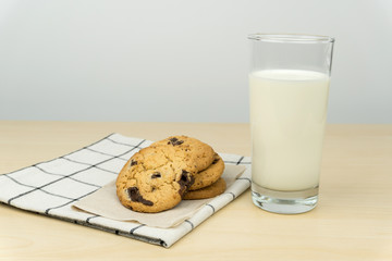 close up of the chocolate chip cookies and a glass of milk at the wooden table.