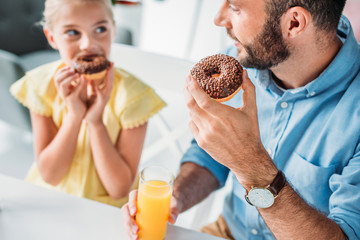 close-up shot of happy father and daughter eating doughnuts with orange juice at home