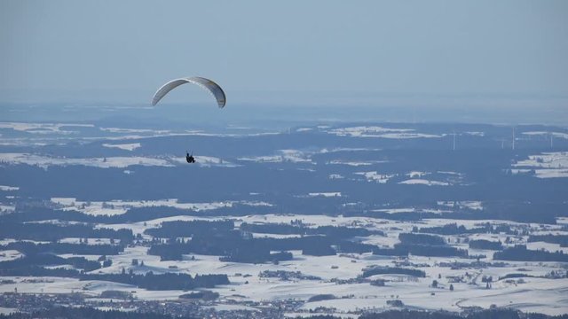 Paraglider circeling over the snow covered landscape of the Allgaeu, Germany, near Fuessen, on the northern edge of the Alps.