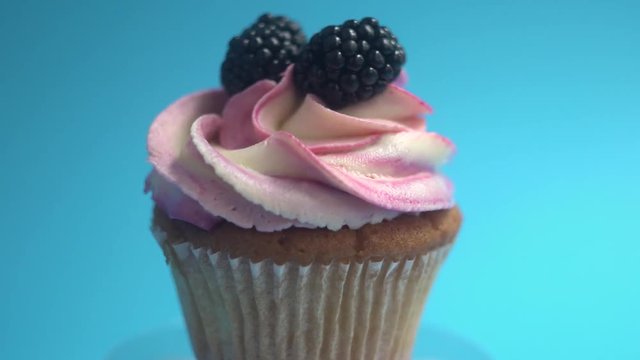 A delicious and appetizing capkake with a pink filling rotates with two blackberries on a blue background.