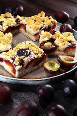 Rustic plum cake on wooden background with plums around.