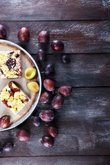 Rustic plum cake on wooden background with plums around.