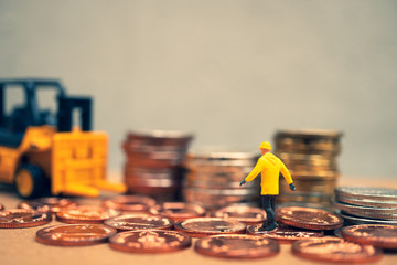 Miniature people, engineer walking on golden stack coins with forklift vehicle background using as finance, industry and business concept - Vintage filter