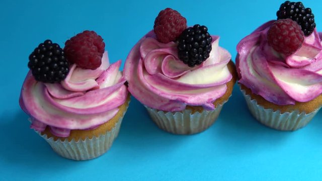 Delicious and appetizing capkake with a pink filling with two berries of blackberries and raspberries on a blue background. Four Cappey Cakes