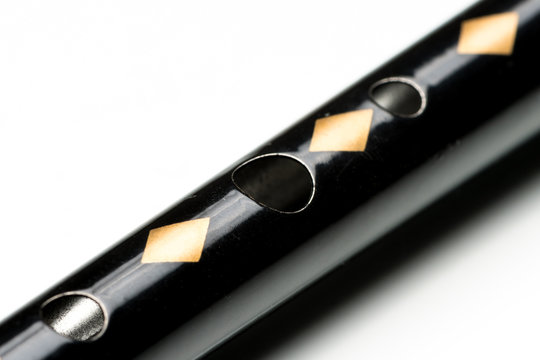 A black tin whistle lying on a white reflective surface