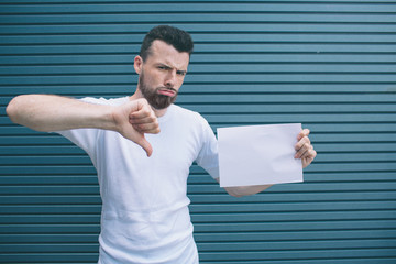 Unhappy man is standing and looking oon camera. He is posing. Guy is holding piece of paper in left...