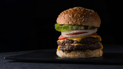 juicy cheeseburger on a flat plate on a black background, close-up