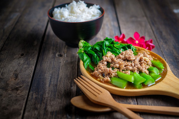 Stir fried Hong Kong kale with pork chops on a wooden table.