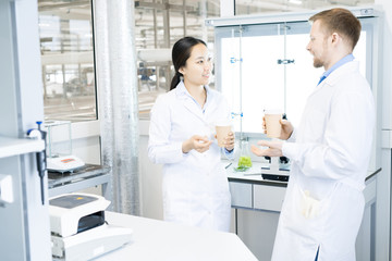 Waist up portrait of two modern young scientists wearing lab coats  chatting while taking break from working in medical laboratory
