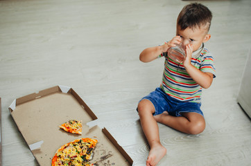 charming boy sitting on the floor eating pizza