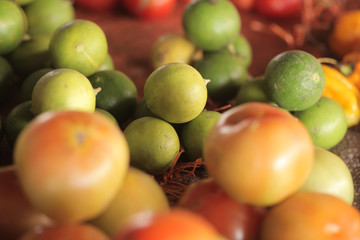 food macro background- many yellow and green limes  and a few tomatoes outdoors on a sunny day in Africa