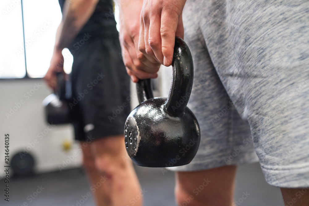 Poster unrecognizable young men in gym doing kettlebell swings.