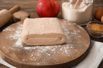Wooden board with raw flaky dough on table