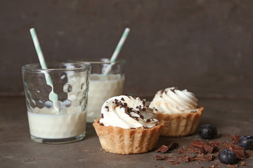 Tasty tartlets with whipped cream and milk on dark background