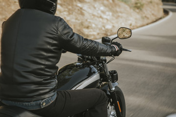 Close up back view of man in black clothes riding an American classic motorcycle.