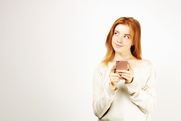 Young beautiful woman with long natural red hair, thinking facial expression and pose holding mobile cell phone. Attractive thoughtful hipster female with smartphone in hands. Background, copy space.