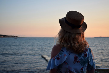 Girl wearing a straw hat is standing by the sea at sunset