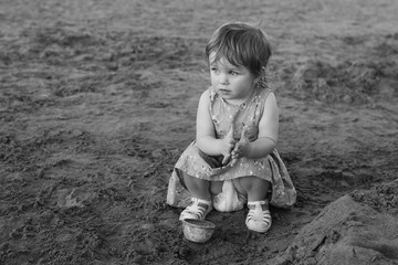 Little caucasian girl have fun digging in the sand at ocean beach, building sand castle.