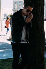 a young guy smokes around a tree in the city.bad habit.smoking in a public place