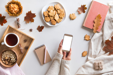 View from above of autumn background with mobile phone, laptop, autumn leaves, cookies, vintage book on white workspace. Top view and flat lay