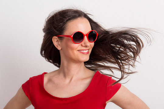 A young beautiful delighted woman with red sunglasses and t-shirt in a studio.