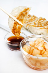 hand with chopsticks holding a piece of  gyoza fried - dumplings snack , with soy sauce