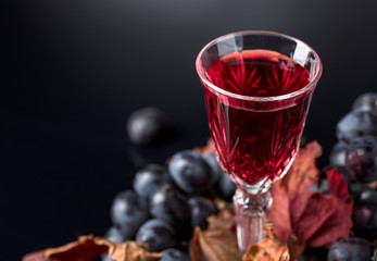 Crystal glass of red wine and grapes with dried vine leaves.