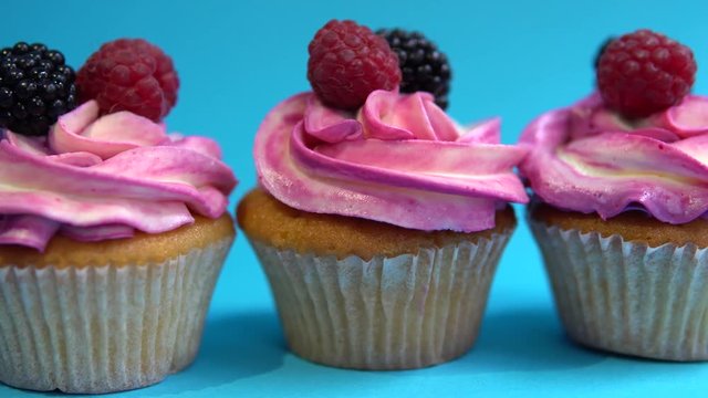 Delicious and appetizing capkake with a pink filling with two berries of blackberries and raspberries on a blue background. Four Cappey Cakes