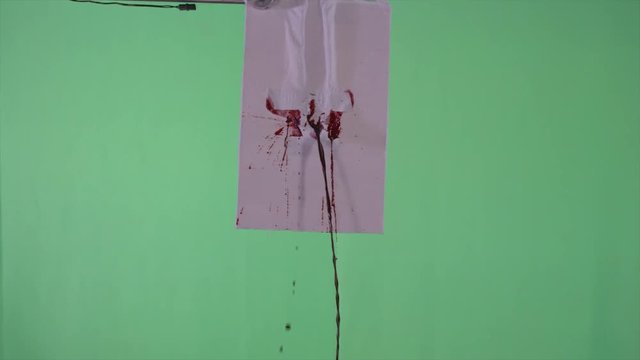 Slow motion frontal close-up of a blood squib exploding through fabric on a green screen. For use with visual effects and/or design and texturing.