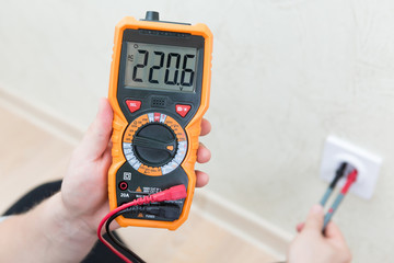 Close-up of man measuring and cheking power supply voltage with digital multimeter
