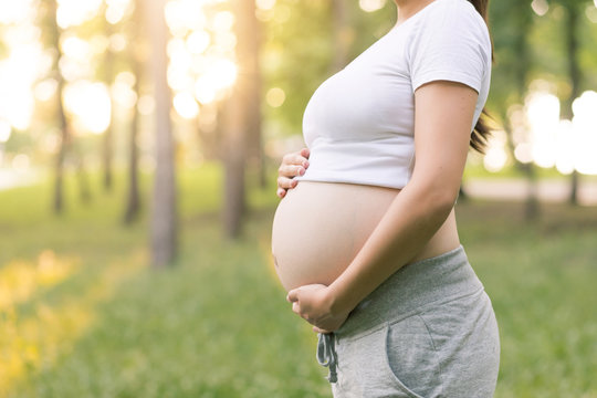 Close-up of belly of Pregnant woman in summer park on the green grass on fit mat, exercising and breathing outdoors. Healthy lifestyle and relaxation concept