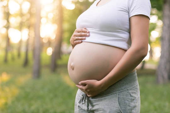 Close-up of belly of Pregnant woman in summer park at sunset, exercising and breathing outdoors. Healthy lifestyle and relaxation concept