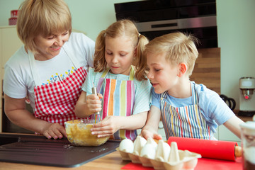 Happy grandmother with her grandchildren having fun during baking muffins and cookies