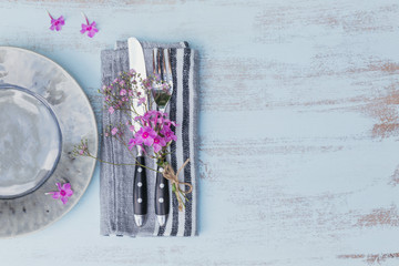 Rustic table setting with pink flowers on light wooden table.