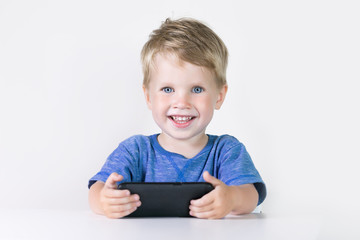 Little kid boy with mobile phone in hands, looking in it and talking on white background. Children...