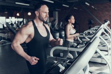 Fototapeta na wymiar Bearded Man and Young Woman on Treadmills in Gym.