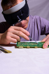 A male engineer is repairing an electronic board. Measurement of parameters and soldering of the electronic board.