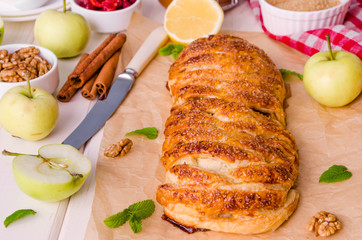 Apple pie with dried cherries, walnuts, lemon zest and cinnamon on white wooden background