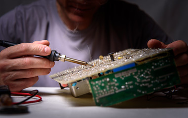 A male engineer is repairing an electronic board. Measurement of parameters and soldering of the electronic board.