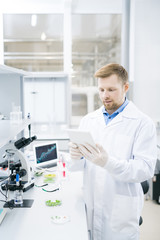 Portrait of focused young scientist wearing lab coat working on research using digital tablet, copy...