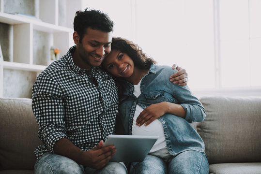 Young Pakistani Man With Pregnant Wife On Sofa.