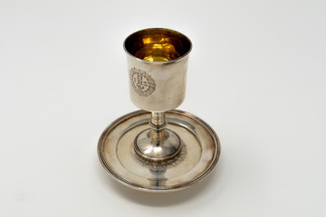 A stirling silver communion chalice to hold the wine during Holy Communion services, with a golden lining and set on top of a silver paten against a white background