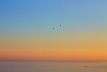 Fototapeta na wymiar Silhouette of powered paraglider soaring flight over the sea against marvellous orange sunset sky.