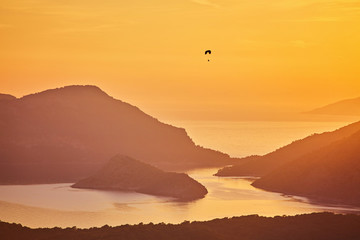 Silhouette of powered paraglider soaring flight over the sea against marvellous orange sunset sky.