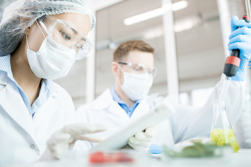 Portrait of two modern scientists wearing masks working on food research studying liquids in beaker...