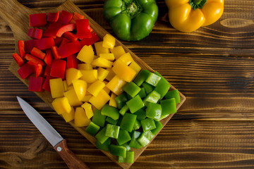 Chopped fresh peppers on the cutting board on the brown wooden background.Top view.