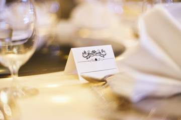 Obraz na płótnie Canvas White blank paper label (mock up) with ornament art for the name on the dinner table with bokeh blurry background
