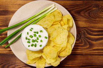 Crispy potato chips with green onion and sour cream on wooden table. Top view