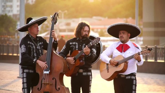 Trio of Mexican musicians mariachi give street concert in the city at sunset. 