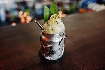 Alcoholic cocktail with ice in can glass on bar table.